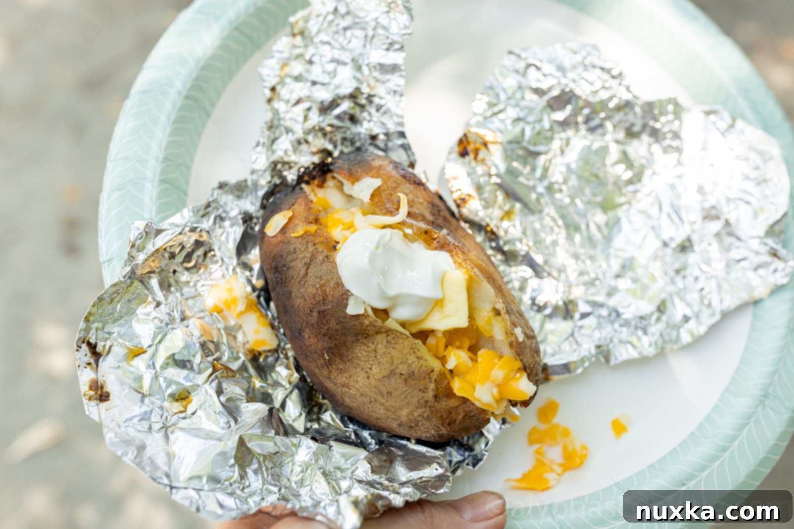 image of a baked potato cooked over a fire on a paper plate unwrapped from foil