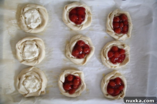 Filled cheese Danish pastries on a baking sheet, with some cream cheese and some canned cherries