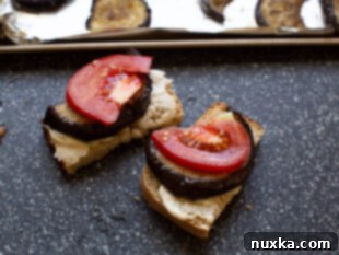 Assembling an open-faced roasted eggplant sandwich with aioli, eggplant, and tomato
