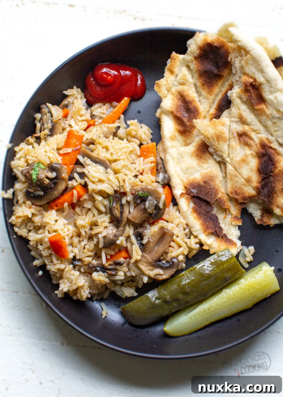 Mushroom rice pilaf served on a plate with unleavened bread, a side of ketchup, and kosher dill pickles.