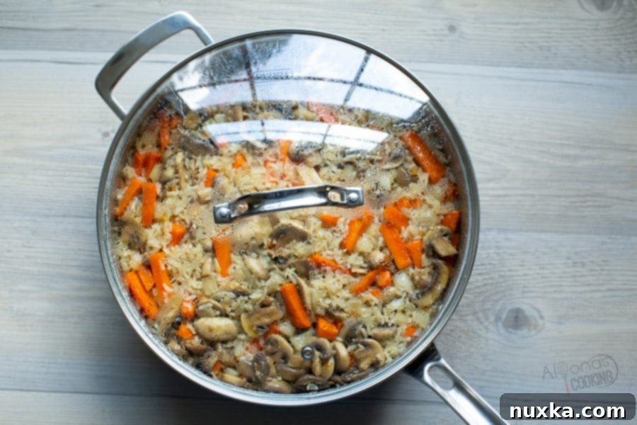 Cooked mushroom rice pilaf in a large pan with the lid slightly ajar, steam gently rising.