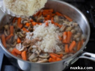 Rinsed rice and seasonings added to sautéed vegetables in a pan.