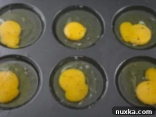 Eggs cracked into muffin tin cavities, seasoned with salt and pepper