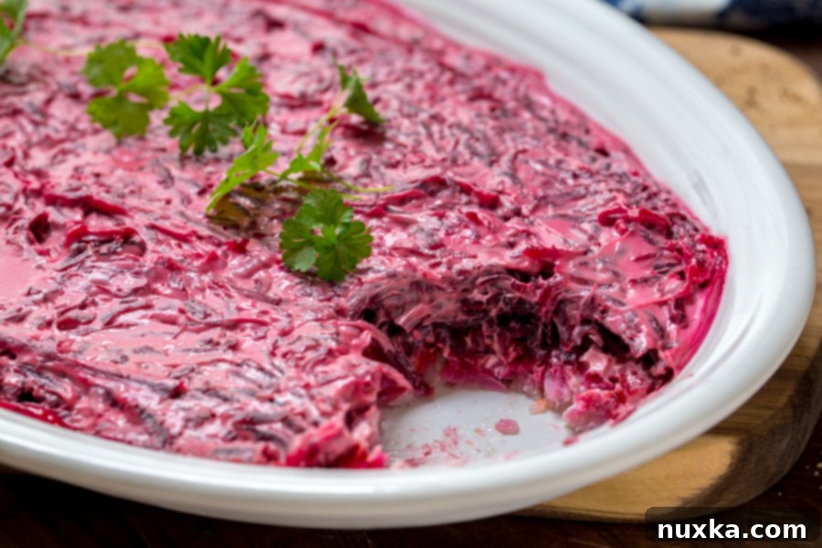 Russian and Ukrainian Shuba Salad layered on a white oval plate with herring fish, potatoes, carrots, beets , and mayo