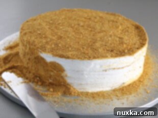 Russian honey cake being assembled on a cake plate, with layers of cake and frosting, and crumbs being applied to the sides
