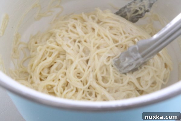 Cream cheese sauce poured over angel hair pasta, ready to be tossed and garnished