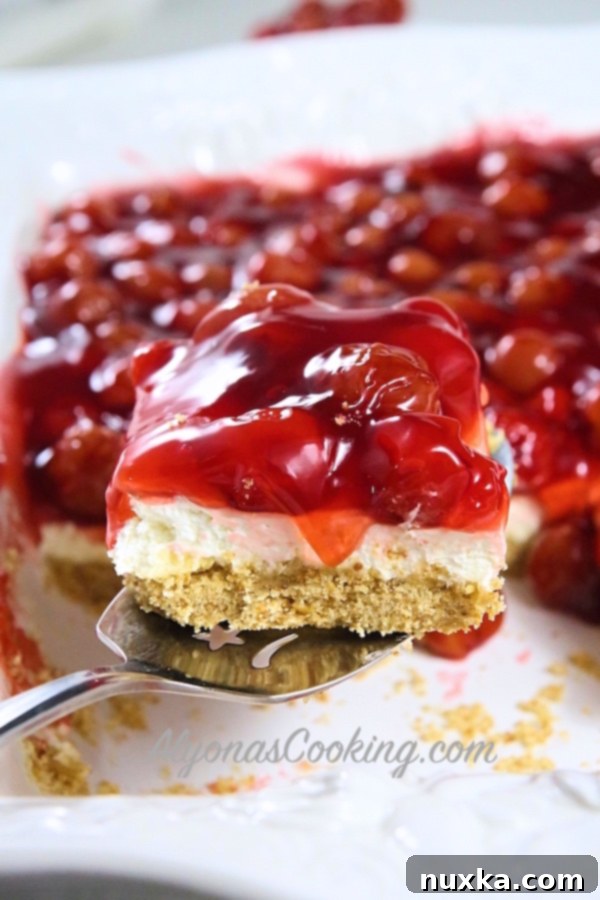 Close-up of a slice of Cherry Pretzel Cheesecake Dessert, showcasing the layers of crust, creamy filling, and cherry topping.