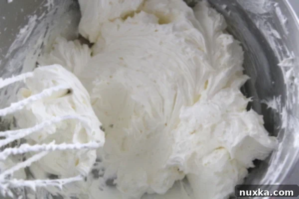 Spreading creamy no-bake cheesecake filling over the cooled pretzel crust in a baking dish.