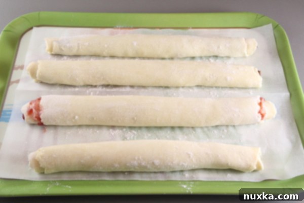 Rolled-up homemade Rugelach dough logs arranged on a parchment-lined tray, ready for an overnight chill.