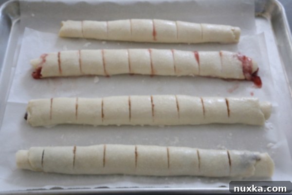 Scored Rugelach dough logs brushed with milk and sprinkled with sugar, ready for baking.