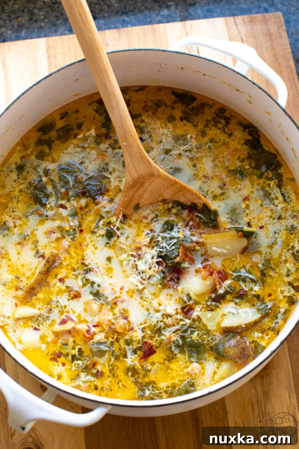 A steaming bowl of Zuppa Toscana soup, garnished with fresh parmesan cheese, ready to be served. Ingredients like Italian sausage, potatoes, bacon, and kale are visible in the creamy broth.