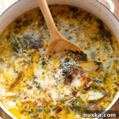 Olive Garden Zuppa Toscana copycat recipe A beautifully presented bowl of Zuppa Toscana, garnished with fresh Parmesan cheese and herbs, ready to be enjoyed. The rich, creamy soup contains Italian sausage, potatoes, bacon, and kale.