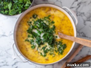 The final step of Zuppa Toscana preparation: a creamy soup being stirred in a pot with fresh kale and a touch of cayenne pepper, ready for serving.