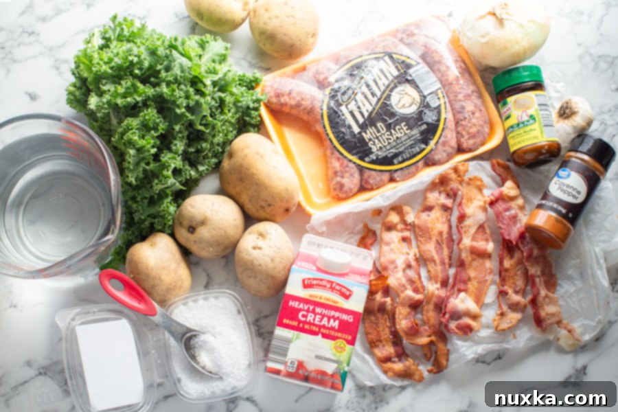 A comprehensive flat lay of Zuppa Toscana ingredients: raw golden potatoes, uncooked bacon slices, a carton of heavy cream, a small bowl of cayenne pepper, chicken bouillon cubes, salt, a glass of water, fresh kale leaves, a whole onion, Italian pork sausage links, and garlic cloves.