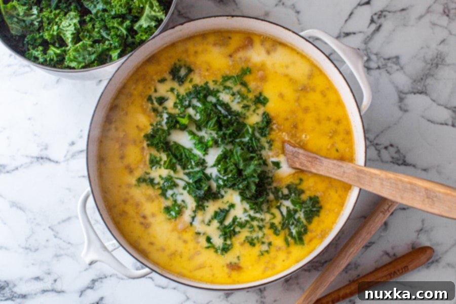 Step-by-step image 3: Heavy cream, fresh chopped kale, and cayenne pepper are stirred into the simmering Zuppa Toscana, brought to a gentle boil, and then removed from heat to preserve the kale's freshness.