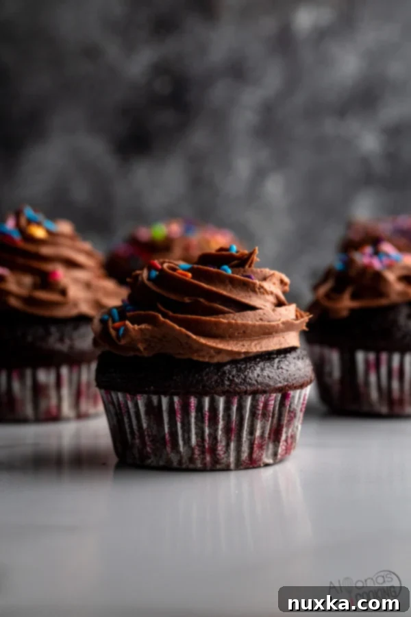 Close-up of a perfectly frosted chocolate cupcake with sprinkles and a mini umbrella, highlighting the rich texture