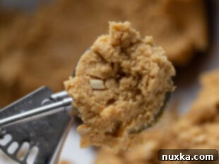 Scooping peanut butter cookie dough onto a baking sheet, spaced out for baking