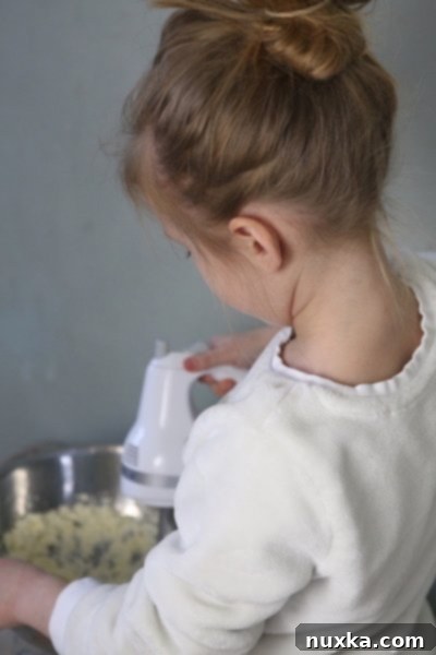 A hand gently rolling a small piece of Nutty Fingers cookie dough into a finger-like shape, ready for baking.