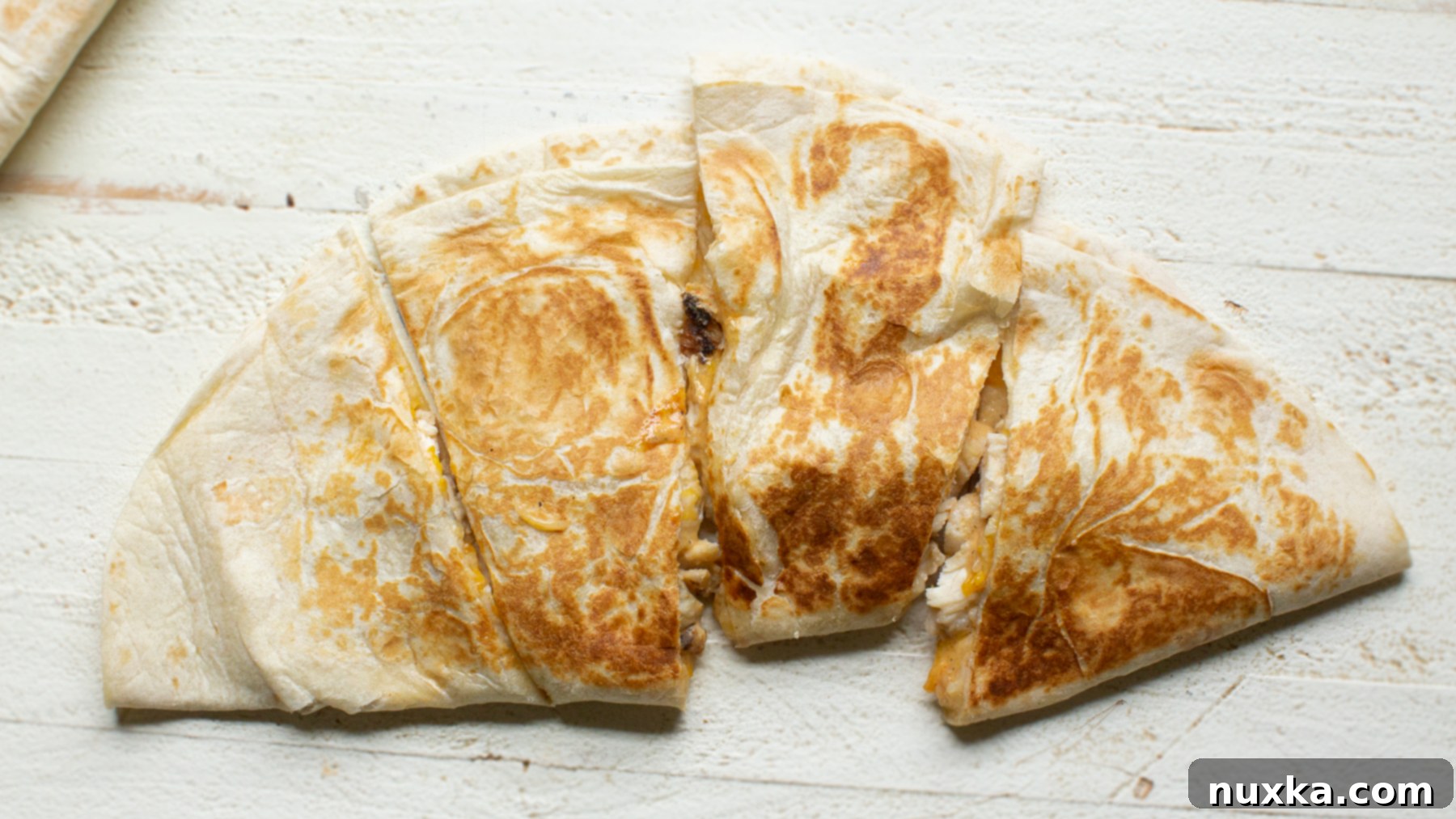 Close-up of golden-brown taco Bell Chicken quesadillas cut into wedges, showing the melted cheese and chicken filling, with a hint of the creamy sauce.