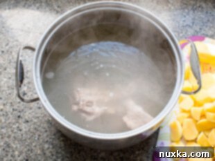 Large pot with water and meat simmering for borscht broth, with dark foam being skimmed off.