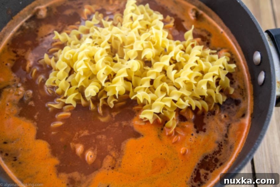 Egg noodles cooking in the beef and sauce mixture in a skillet