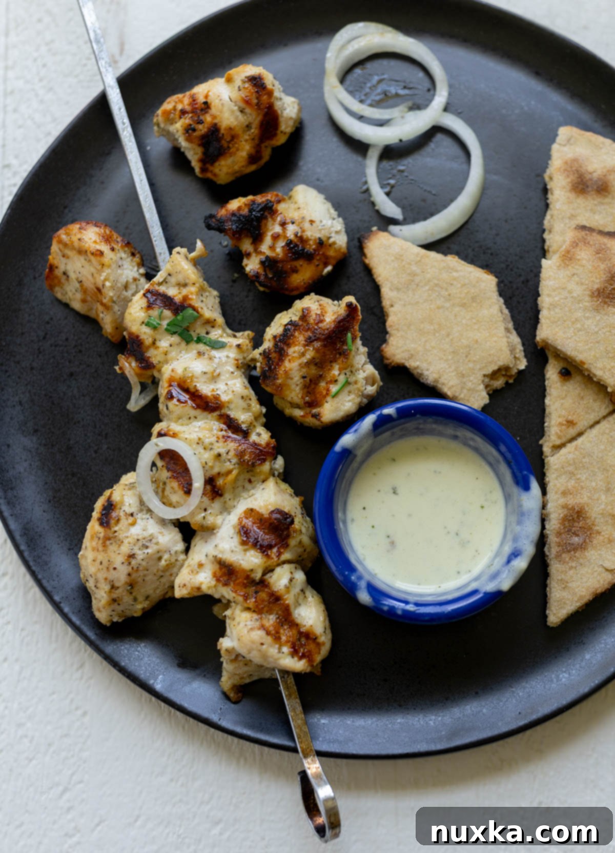 serving chicken kabobs on a plate with flatbread, sliced onions, and a side of ranch dressing
