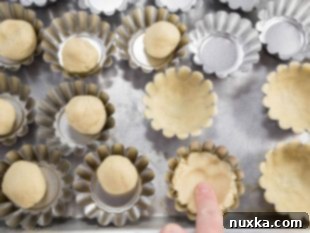 Shortbread cookie dough being molded into mini tart tins to create the basket shape.