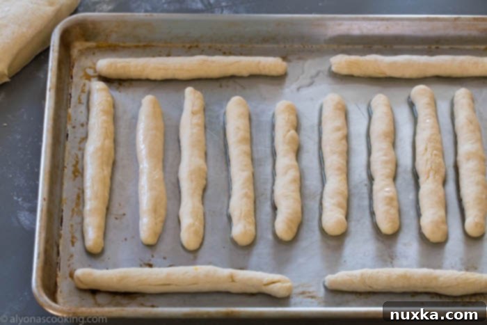 Rolled out breadstick dough pieces arranged on a baking sheet