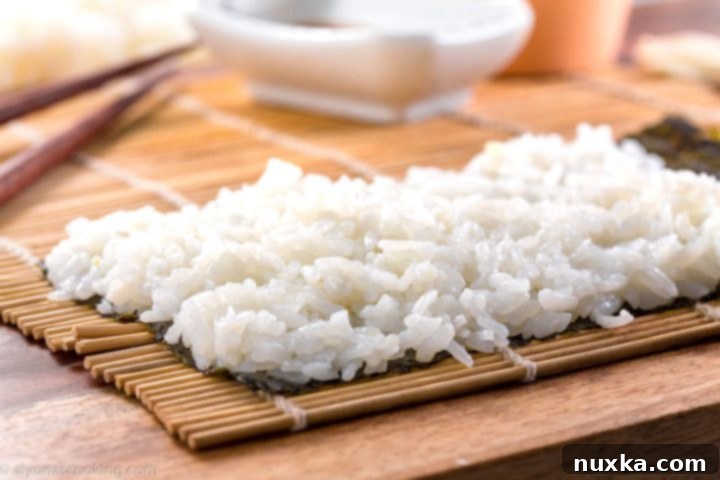 Sticky sushi rice spread on a sheet of dried seaweed on a bamboo sushi mat, ready for rolling.