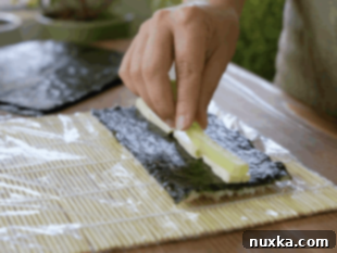 Adding cream cheese and cucumber to sushi roll