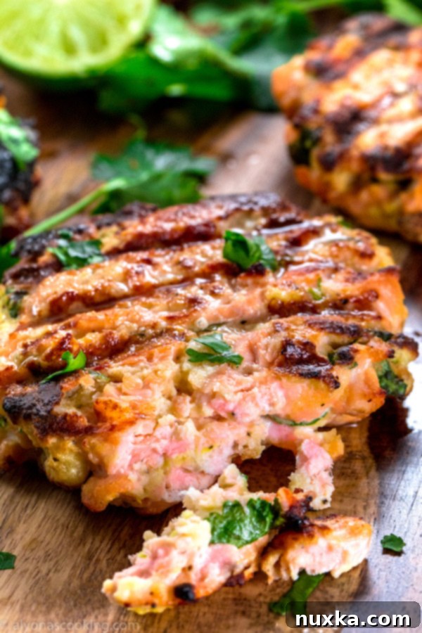 A close-up of a grilled salmon burger patty, showcasing its rustic texture and flecks of fresh herbs, ready for toppings.
