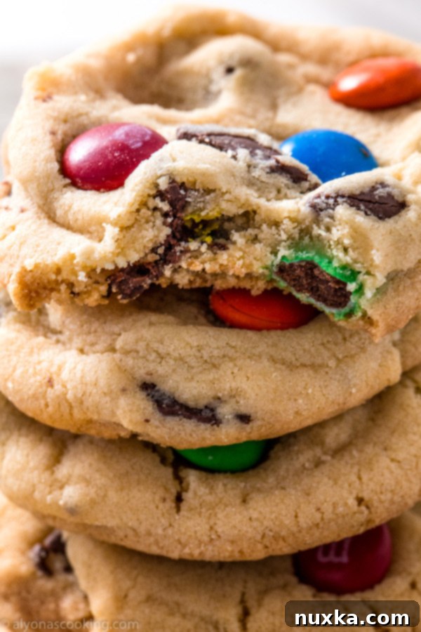 A stack of golden brown M&M cookies, showcasing their chewy texture and colorful candy