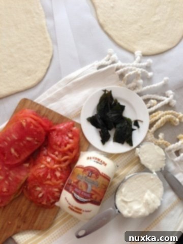 Fresh white pizza topping ingredients: sliced mozzarella, tomatoes, basil, and white sauce