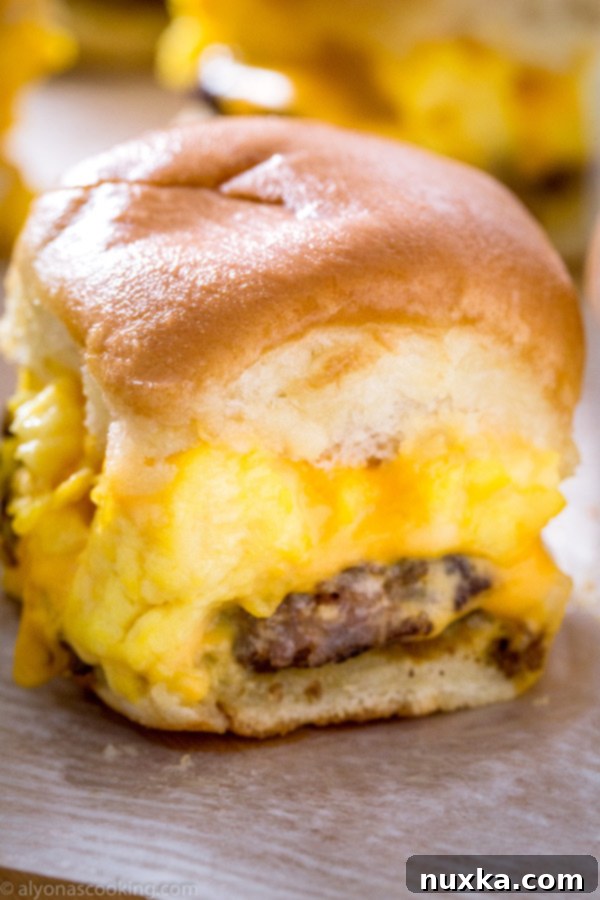 A close-up of a single Sausage, Egg, and Cheese Breakfast Slider, showing the fluffy egg, savory sausage, and melted cheese inside a soft dinner roll.