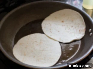Heating tortillas in a skillet with oil for crispy breakfast quesadillas.