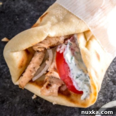Plated homemade chicken gyros with pita, chicken, and a side of tzatziki