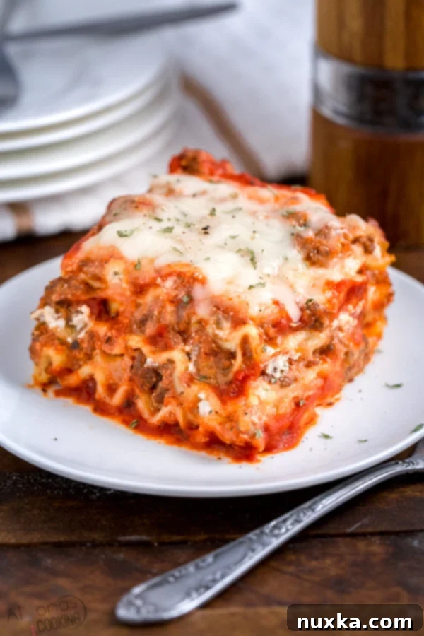 A perfectly portioned slice of classic meat sauce lasagna on a white plate, garnished with fresh parsley, showing distinct layers of pasta, rich meat sauce, and melted cheese.