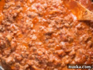 Ground beef lasagna meat sauce simmering in a pan with marinara and ricotta cheese.