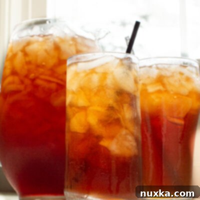 A refreshing glass of homemade iced tea with lemon slices and ice, alongside a pitcher of freshly brewed tea, perfect for cooling down on a warm day.