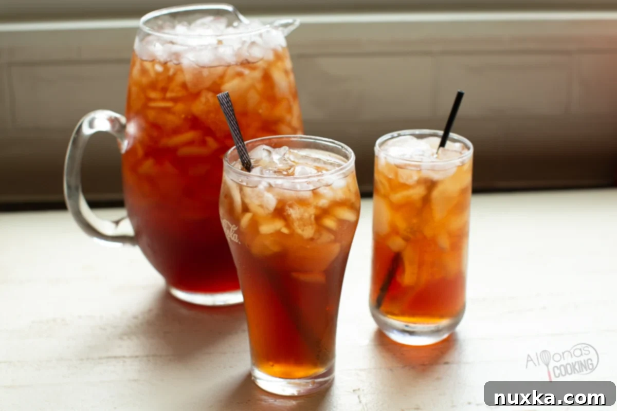 A refreshing glass of homemade iced tea with lemon and ice, next to a full pitcher, showcasing perfect chilling.