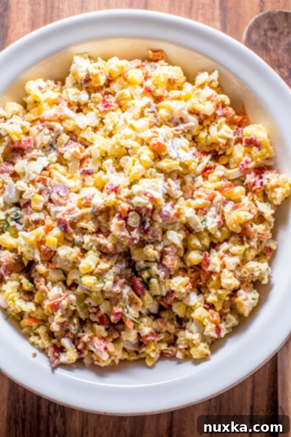 A large bowl of creamy bacon potato salad, garnished with fresh dill and a spoon for serving.