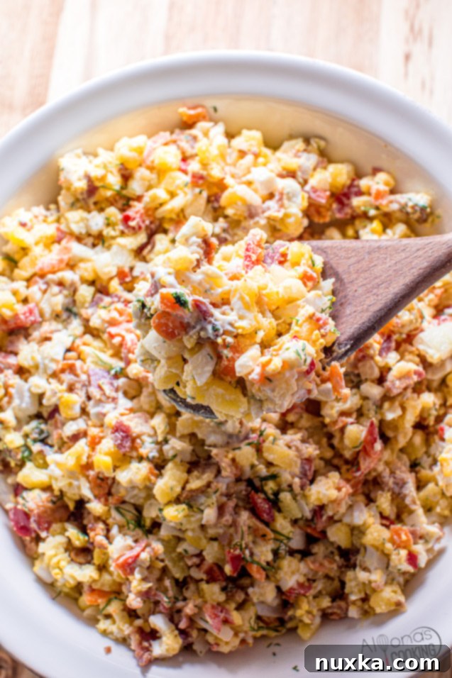 A close-up shot of the creamy bacon potato salad with visible pieces of bacon, corn, bell pepper, and dill.