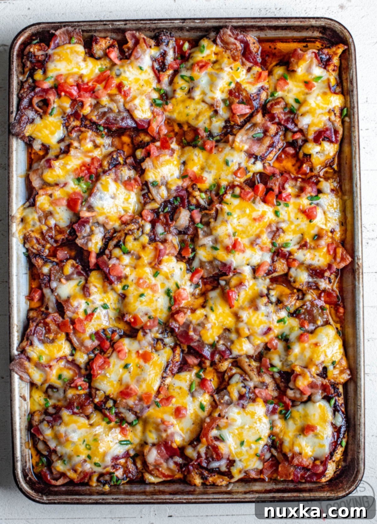 cheesy bacon BBQ chicken on a baking sheet baked from the oven. This Monterey chicken is a Chilis inspired dish topped with bbq sauce, bacon, Monterey Jack cheese, and tomatoes