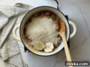 Step 4: Layering rice and garlic over beef and vegetables, then pouring in broth.