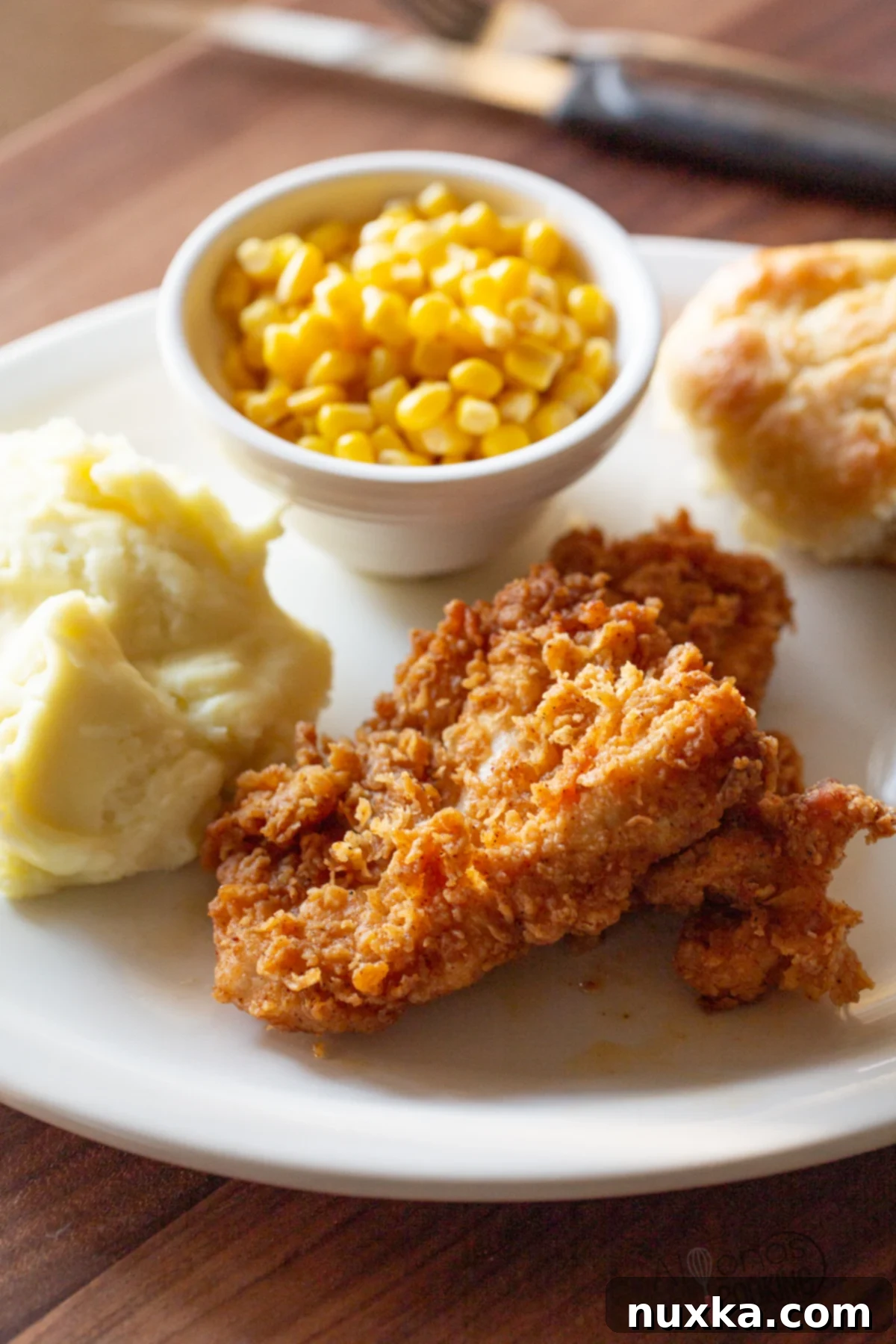 Country fried chicken recipe served with country gravy and a side of mashed potatoes, cranberry sauce, and honey-glazed biscuits