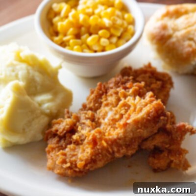 Country fried chicken recipe served with country gravy and a side of mashed potatoes, cranberry sauce, and honey-glazed biscuits
