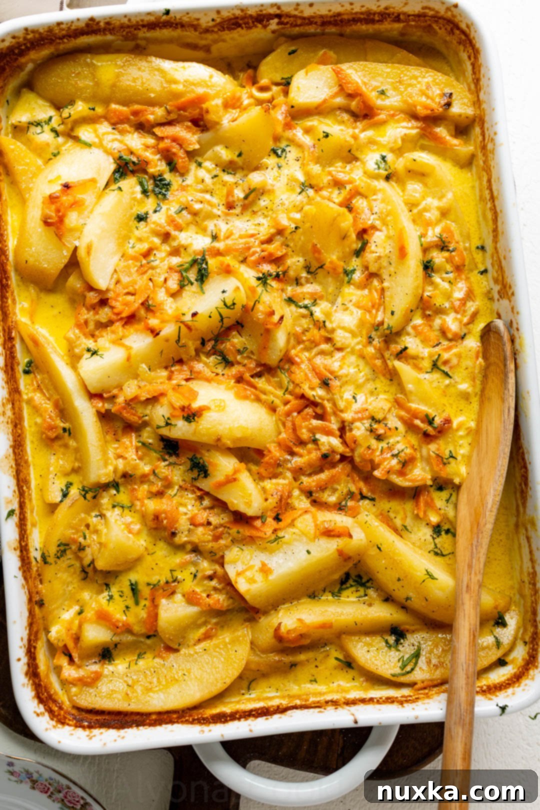 Cream-Infused Baked Potato Wedges 4 creamy baked potato wedges in heavy cream sauce with carrots and onions sprinkled with dill in a casserole dish ready to serve