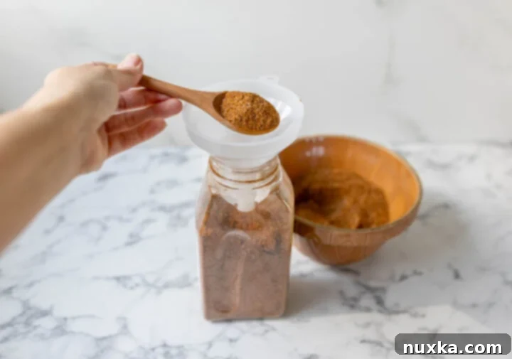 A hand transferring homemade taco seasoning into a bulk spice container for storage.