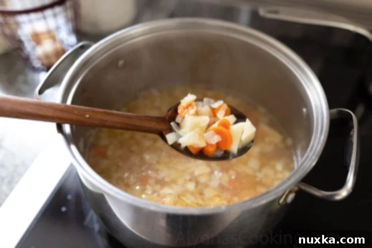 Carrots, potatoes, and broth simmering in a pot for a creamy chicken chowder base.