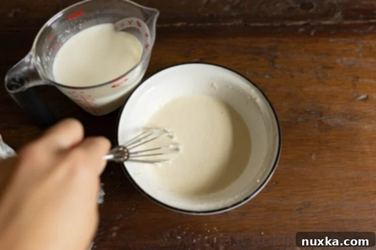 Making a smooth slurry with flour and milk in a bowl for thickening chicken chowder.